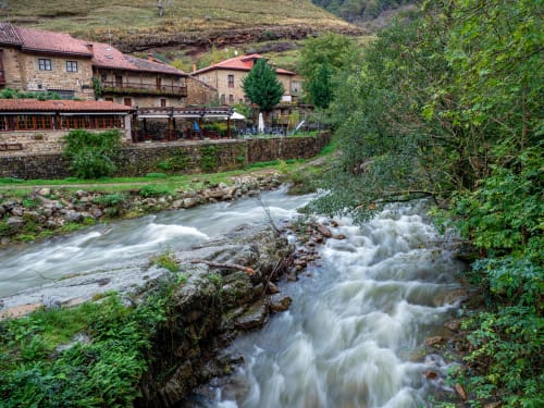 Rushing river beside stone buildings with terracotta roofs at Posada La Colodra in Spain