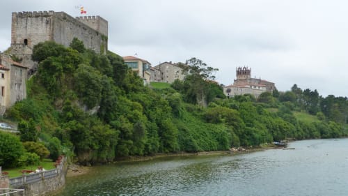 Medieval castles perched on lush green cliffs overlooking a calm river in Spain