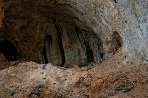 Ancient cave dwelling entrance at Posada La Colodra with weathered rock formations and sandy ground, Spain