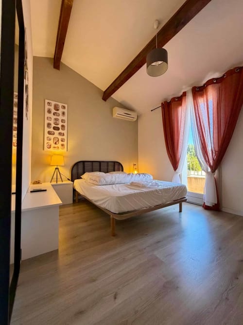 Chambre moderne aux Villas d'A Storia à Porto-Vecchio avec lit, poutres en bois, rideaux rouges et vue sur la baie