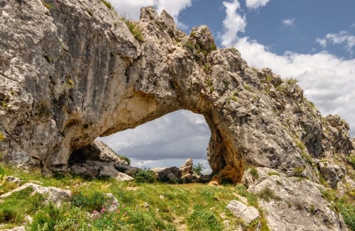 Natürliche Felsbogenformation mit grünem Gras und Wildblumen bei Casa Gallinera in Benissivà, Spanien