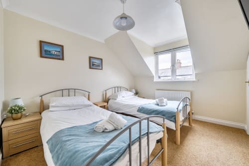 Bright twin bedroom at Archies Place cottage in Padstow with metal bed frames, white linens, and garden views from dormer