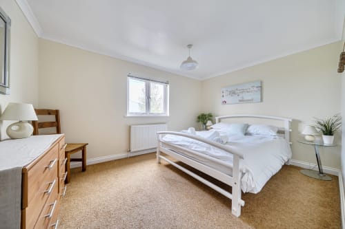 Bright bedroom at Archies Place cottage in Padstow with white bed, wooden dresser, and garden views
