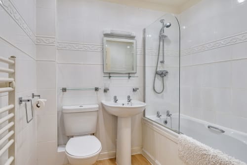 Modern white bathroom with pedestal sink, toilet, heated towel rail, and shower-bath enclosure at Archies Place cottage in
