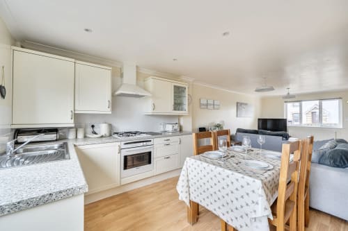 Open-plan kitchen and dining area in Archies Place cottage, Padstow, with cream cabinets and wooden dining table