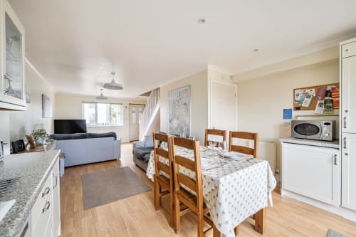 Open-plan kitchen and dining area in Archies Place cottage, Padstow, with wooden table, staircase, and garden view
