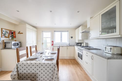 Bright kitchen-dining area at Archies Place cottage in Padstow with cream cabinets, dining table set for guests, and garden