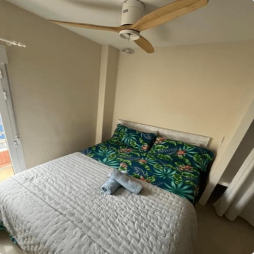 Dormitorio del apartamento Algemesi Home con ventilador de techo de madera, ropa de cama blanca, almohadas con estampado tropical y vistas a la ciudad.