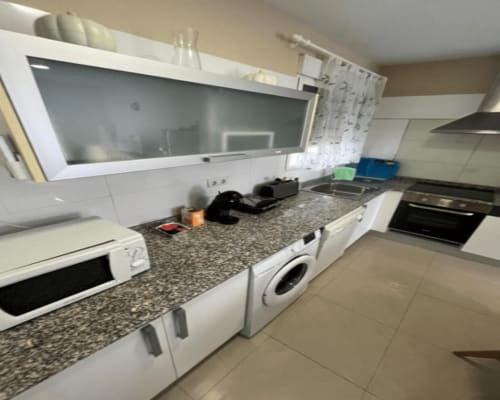 Modern apartment kitchen at Algemesi Home with white cabinets, granite countertop, appliances, and washing machine.