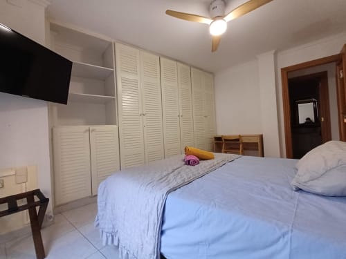 Bright bedroom in Algemesi apartment with blue bed, white louvered wardrobes, ceiling fan, and TV