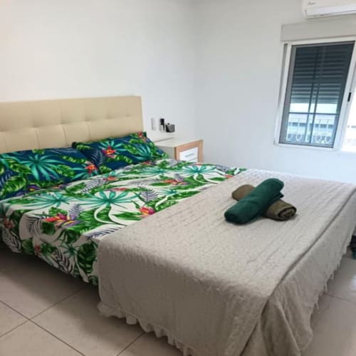 Dormitorio luminoso en Algemesi Home con ropa de cama tropical, cabecero crema y vistas a la ciudad de San Jose Luminoso