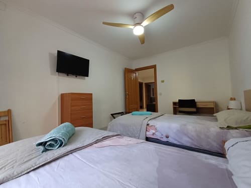 Bright bedroom with two beds, ceiling fan, TV, wooden dresser, and door at Algemesi Home apartment in Spain