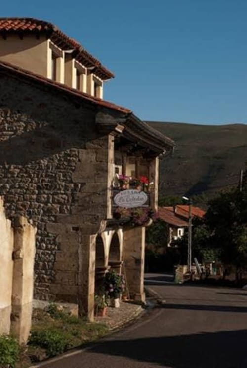 Posada La Colodra stone hotel facade with red tile roof and wooden shutters in Los Tojos, Spain