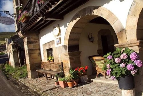 Posada La Colodra entrance with arched doorway, flowering plants, and rustic stone courtyard in Los Tojos