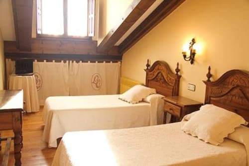 Twin bedroom at Posada La Colodra hotel in Los Tojos with wooden beds, cream bedding, and sloped ceiling