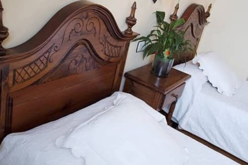 Ornate wooden bed with white linens at Posada La Colodra, featuring carved headboard and nightstand with fresh flowers