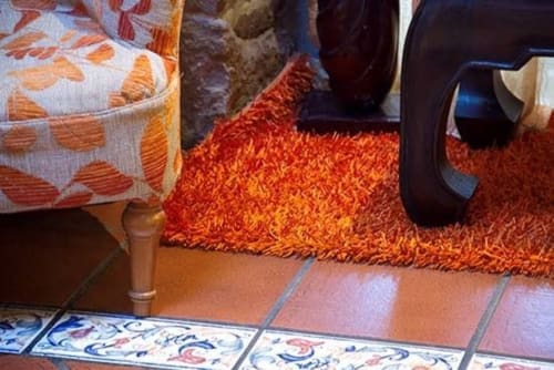 Cozy interior at Posada La Colodra with orange rug, patterned ottoman, and decorative tile flooring in Los Tojos