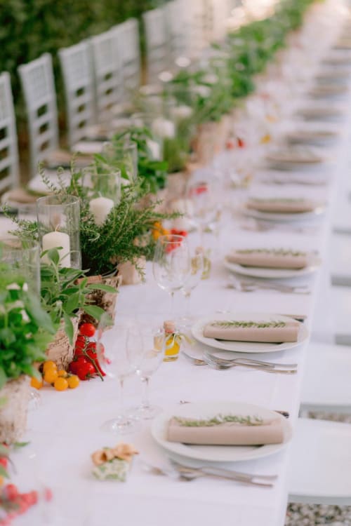Elegante tavolo per banchetto all'aperto a Borgo di Erboli con mise en place, tovaglioli bianchi e decorazioni di erbe aromatiche e bacche fresche