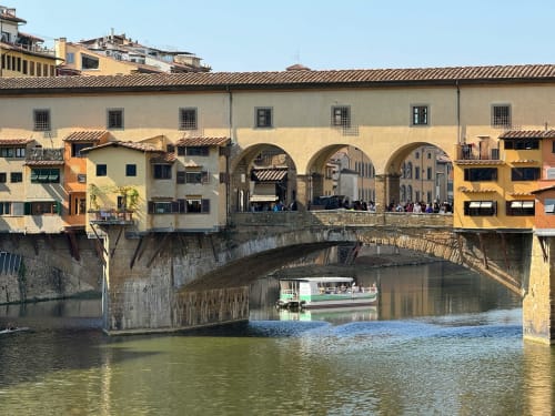 Ponte Vecchio-style arched bridge over Arno River with colorful Renaissance buildings in Cavriglia, Italy