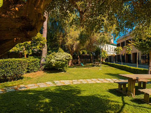 Cortile del Palazzo Sebeto a Napoli con lussureggiante vegetazione, alberi alti, panche in legno e facciata in terracotta