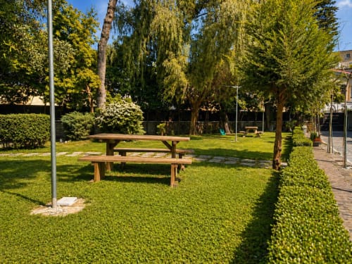 Tavoli da picnic in legno nel rigoglioso giardino di Palazzo Sebeto, hotel di Napoli con alberi maestosi e siepi curate