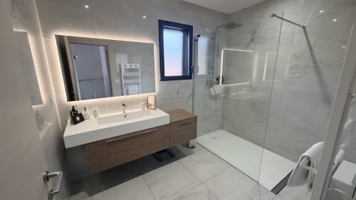 Modern bathroom in Villa Capu Biancu, Corsica with illuminated mirror, marble tiles, floating vanity, and walk-in shower