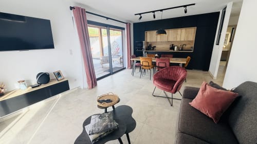 Modern open-plan living area in Villa Capu Biancu, Corsica, featuring dark accent wall, burgundy armchairs, gray sofa,