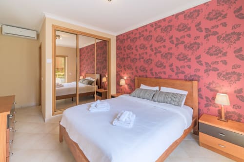 Camera da letto spaziosa presso l'Apartamento Golfinho a Portimão con letto in legno, carta da parati floreale rossa, armadio con specchio e stile moderno