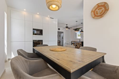 Comedor moderno en Villa Olsson Ayma con mesa de madera, sillas grises y cocina abierta con muebles blancos