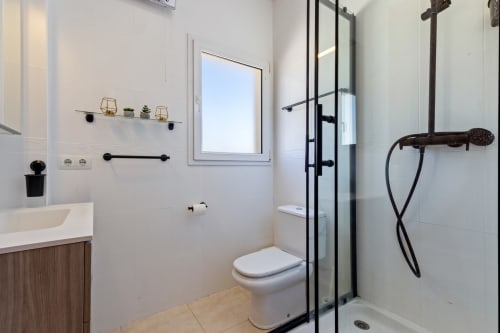 Baño moderno de villa con ducha a ras de suelo, inodoro, lavamanos y accesorios en negro en Alhaurín de la Torre