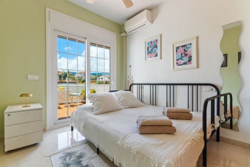 Dormitorio luminoso en Ayma Villa Olsson con cama negra, ropa de cama blanca, puertas de terraza con vistas a la piscina y detalles verde lima