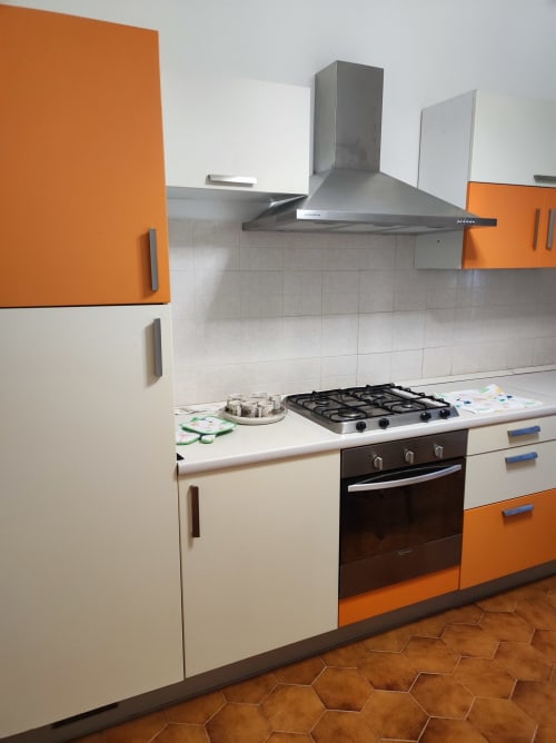 Cucina moderna con mobili arancioni e bianchi, piano cottura a gas e cappa acciaio inox all'appartamento MAISON PLATONE JOLIE