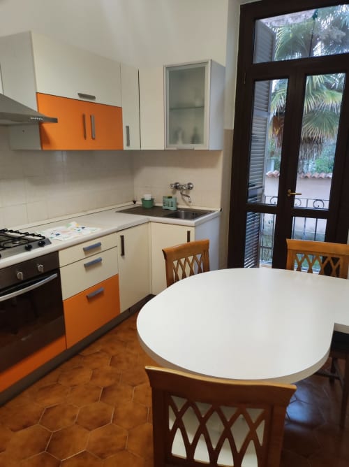 Cucina moderna con mobili arancioni e bianchi, tavolo rotondo e porte con vista sul giardino a MAISON PLATONE JOLIE