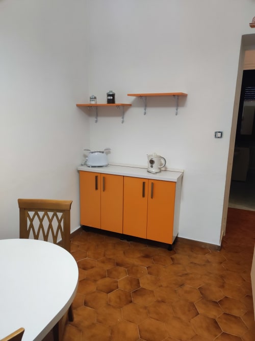 Cucinetta moderna con mobili arancioni, piano di lavoro bianco e scaffalature nell'appartamento Maison Platone Jolie ad Alessandria