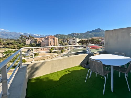 Terrasse moderne sur toit avec gazon synthétique, table et chaises blanches, vues sur les montagnes et la mer à L'Île-Rousse, Corse