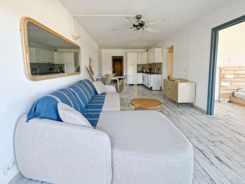 Séjour moderne avec canapé rayé bleu, miroir en bois, coin cuisine et vue mer à L'Île-Rousse