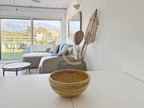 Salon contemporain avec bol en bois, vue sur mer par portes vitrées, paysage montagneux et terrasse aménagée à L'Île-Rousse