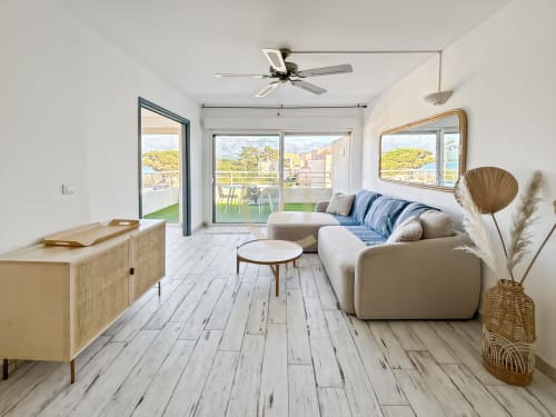 Appartement moderne à L'Île-Rousse avec vue mer, canapé beige, meubles bois, ventilateur plafonnier et accès à terrasse face à la plage