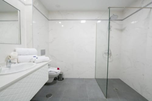 Salle de bains moderne à l'Aevum Resort avec murs en marbre, douche à l'italienne, lavabo et serviettes blanches