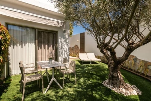 Suite terrazza Aevum Resort avec patio meublé, olivier, transats et bâtiment blanc moderne à Playa del Inglés