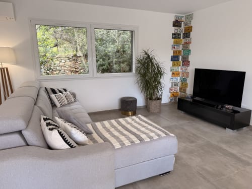 Modern villa living room in Figari with grey sofa, striped rug, TV, license plate wall art, plants, and mountain views