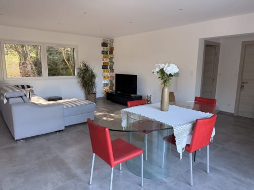 Modern villa living space with dining area, red chairs, glass table, light sofa, TV, white flowers, mountain views in Figari