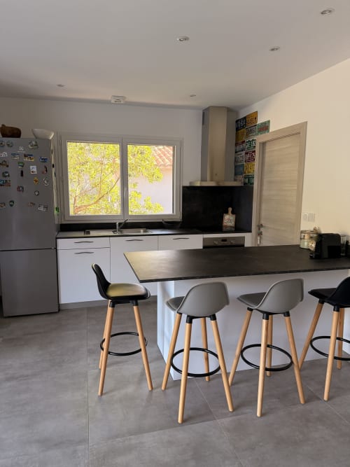 Modern kitchen with black countertop island, bar seating, white cabinetry, and large windows overlooking greenery at Villa A