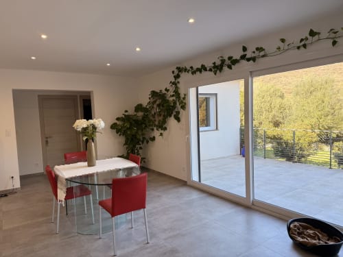 Modern dining area in A Santa villa, Figari, with red chairs, glass table, mountain views through sliding doors, and