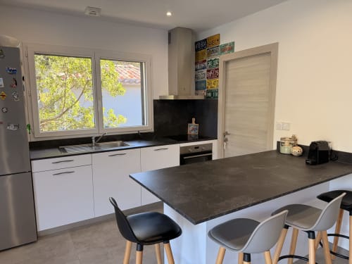 Modern kitchen in A Santa villa, Figari with white cabinetry, dark countertop, island seating, and mountain views through