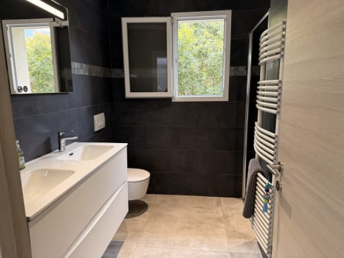 Modern bathroom at In Casa Conciergerie villa in Figari with white vanity, black tile walls, heated towel rack, and view of