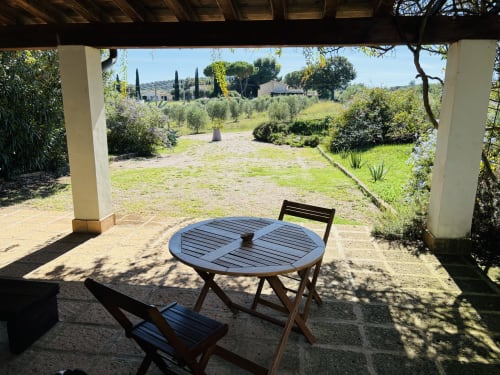 Patio sombreado con mesa redonda y sillas con vistas a olivares en Casale Artemisia, Capalbio