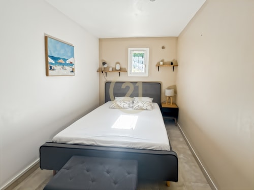 Chambre moderne de l'appartement à L'Île-Rousse avec lit noir, literie blanche, murs beige, étagères et décor marin
