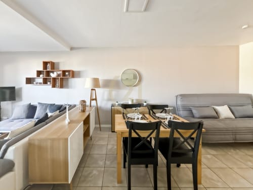 Appartement moderne à L'Île-Rousse avec table à manger, canapé gris, étagères bois et accès balcon vue mer