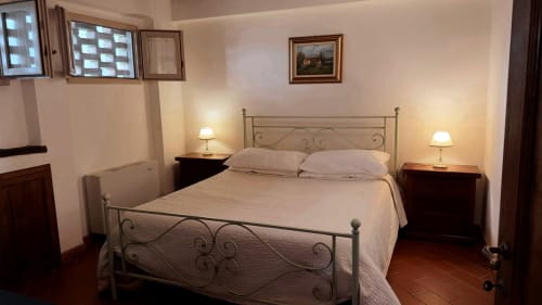 Accogliente camera da letto con letto in ferro battuto, comodini gemelli con lampade e pavimenti in cotto a Borgo di Erboli a Cavriglia, Italia